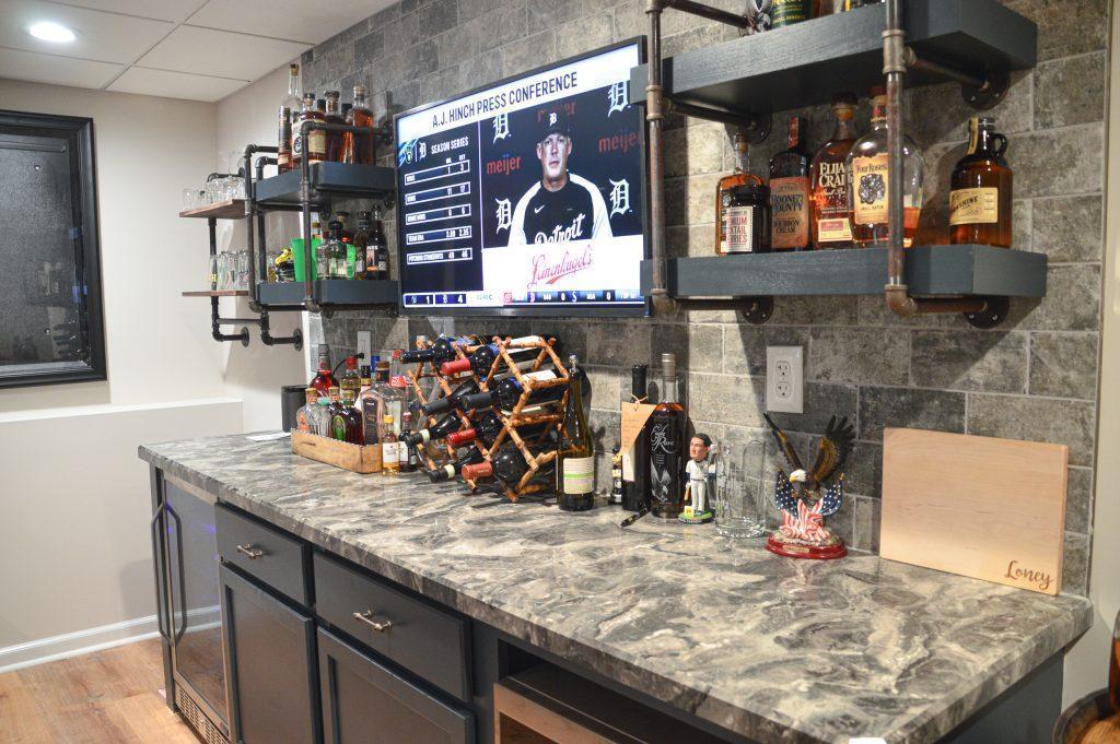 Finished basement bar area with nice backsplash, shelving holding liquor and wine bottles and a tv for entertainment.