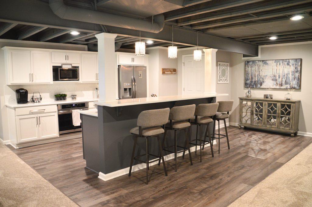 Finished basement bar rea with seating for four, overlooking the living room area, also displaying the dryfall ceiling. .