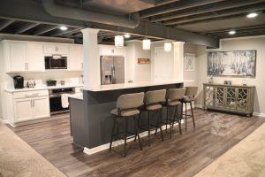 Finished basement bar rea with seating for four, overlooking the living room area, also displaying the dryfall ceiling. .