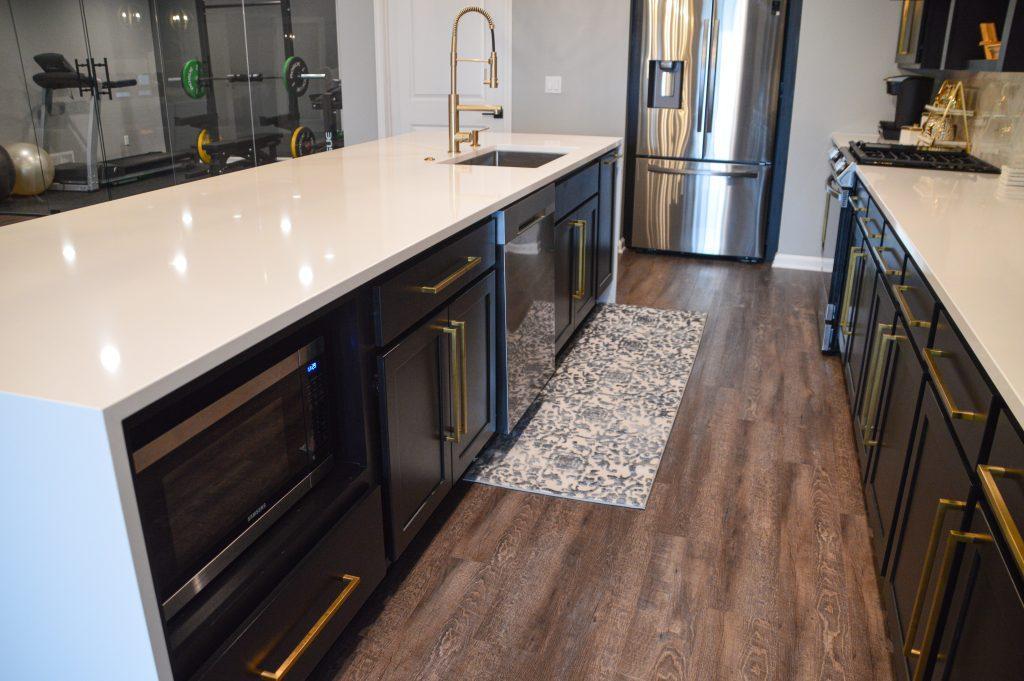 View of the long white quartz countertop in the kitchen area with black cabinets below and gold hardware.