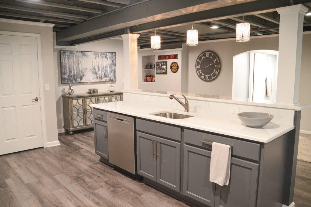 Finished basement bar area from behind the bar showing off storage cabinets, wall art and decorative table.