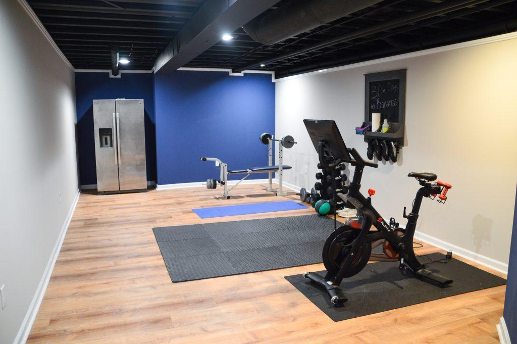 Finished basement home gym with peloton, weights and fridge.