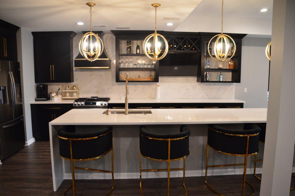 Kitchen area with long white counter island, black cabinets over the back counter, and gold hanging lights.