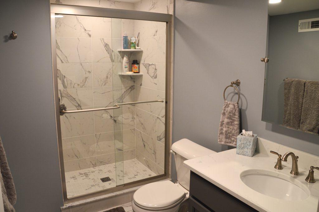 Finished basement bathroom with walk-in shower that has decorative tile, vanity and white countertop.