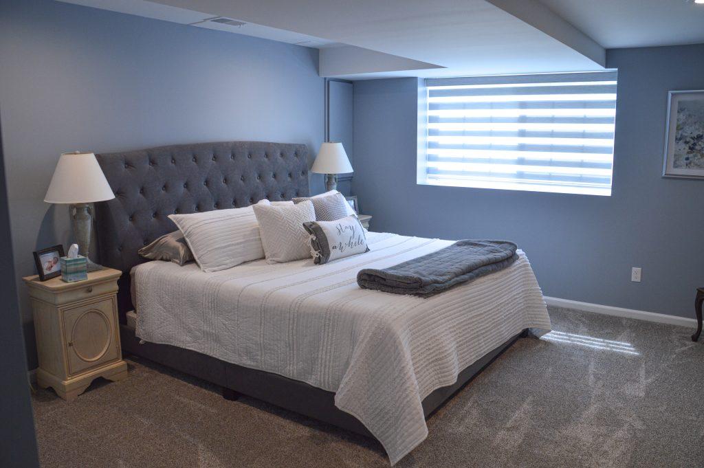 Finished basement guest room with drywall ceiling and large bed for guests.