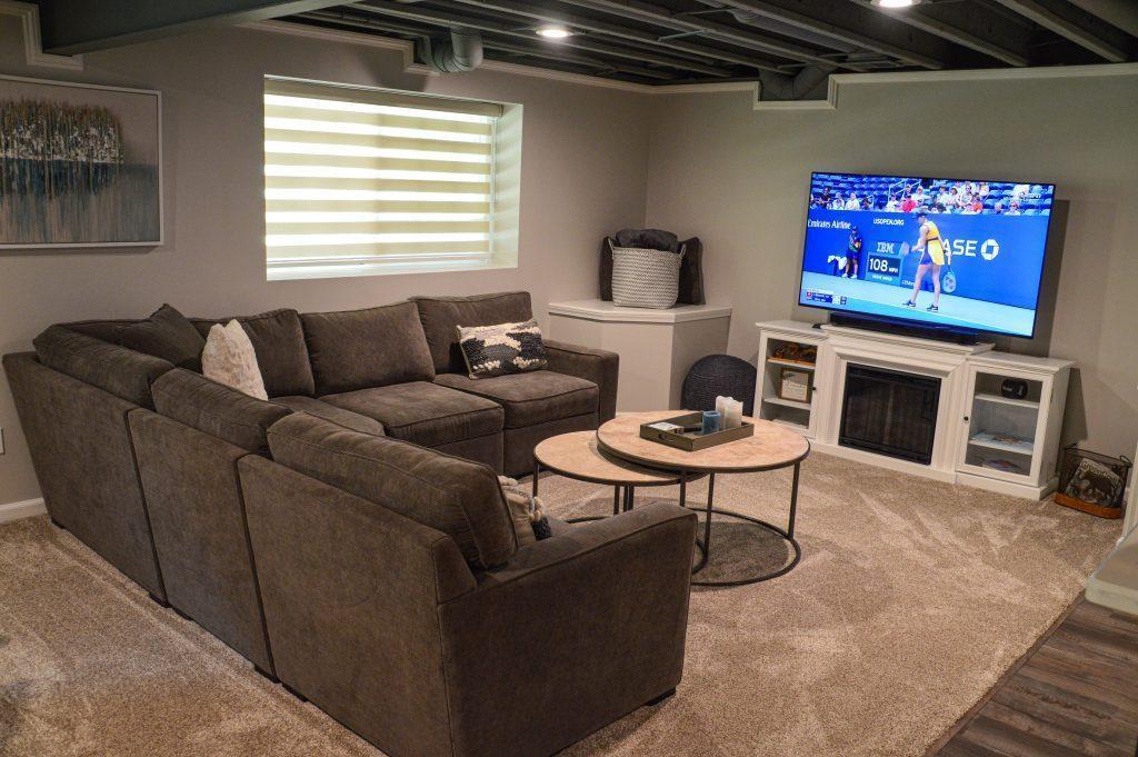 Finished basement overlooking the living room area with TV, electric fireplace and sump pump cover.