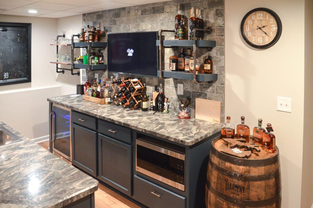 Finished basement bar area with nice backsplash, shelving holding liquor and wine bottles and a tv for entertainment.