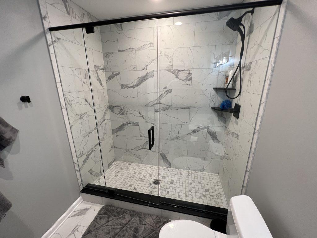 View of the walk-in shower with glass swing door and stone tiles inside.