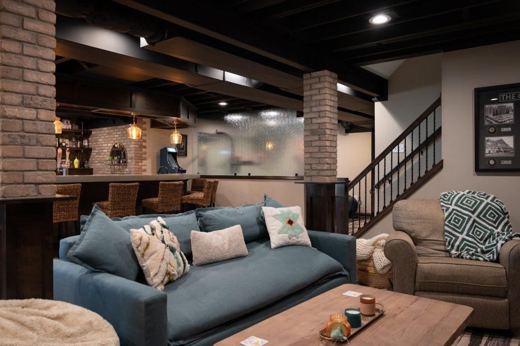 Finished basement view from the tv wall overlooking the seating area, stairs from main level, bar and home gym.