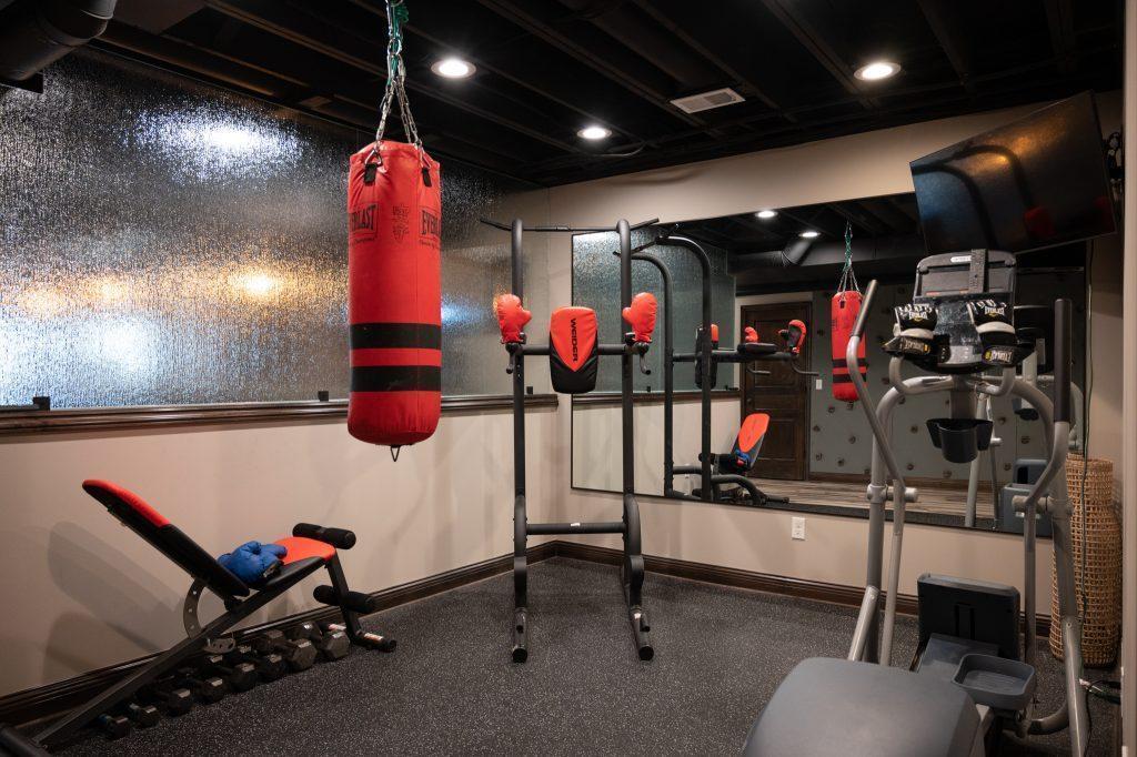 Finished basement home gym with tempered glass on top of a half wall that separates the gym and home bar.