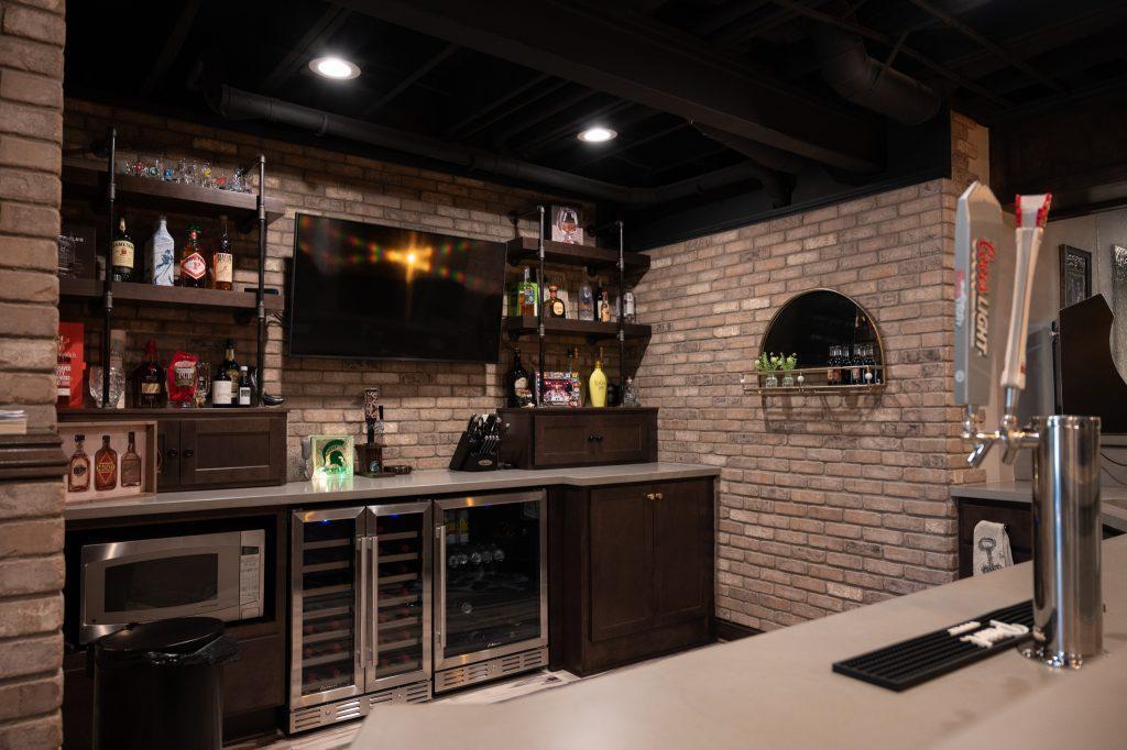 Finished basement bar view of the back wall with shelving, tv and brick panel accent walls.