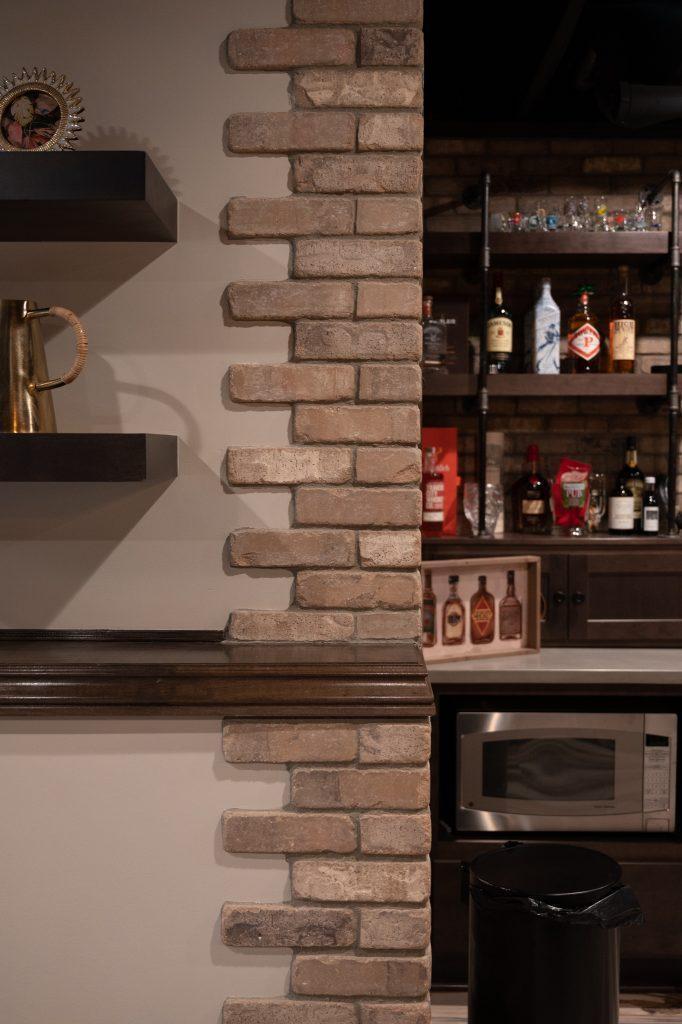 Finished basement bar area close up of a corner with brick overlaying the drywall with a jagged zipper look.