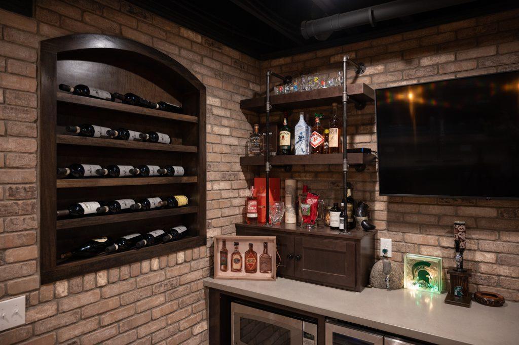 Finished basement bar area closeup of left wall and back of the bar displaying custom built-in wine shelving on the left and shelving for spirits on the back wall.