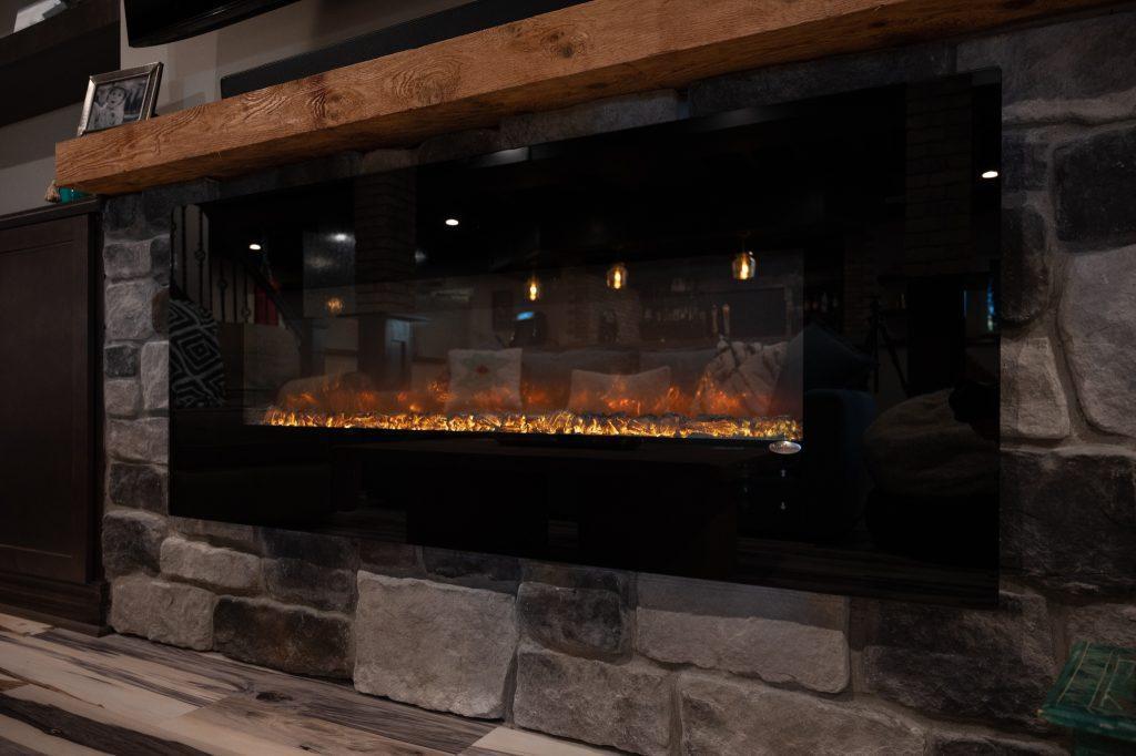 Closeup look of the electric fireplace under the tv in the living room area with stone backsplash and wooden mantel above.