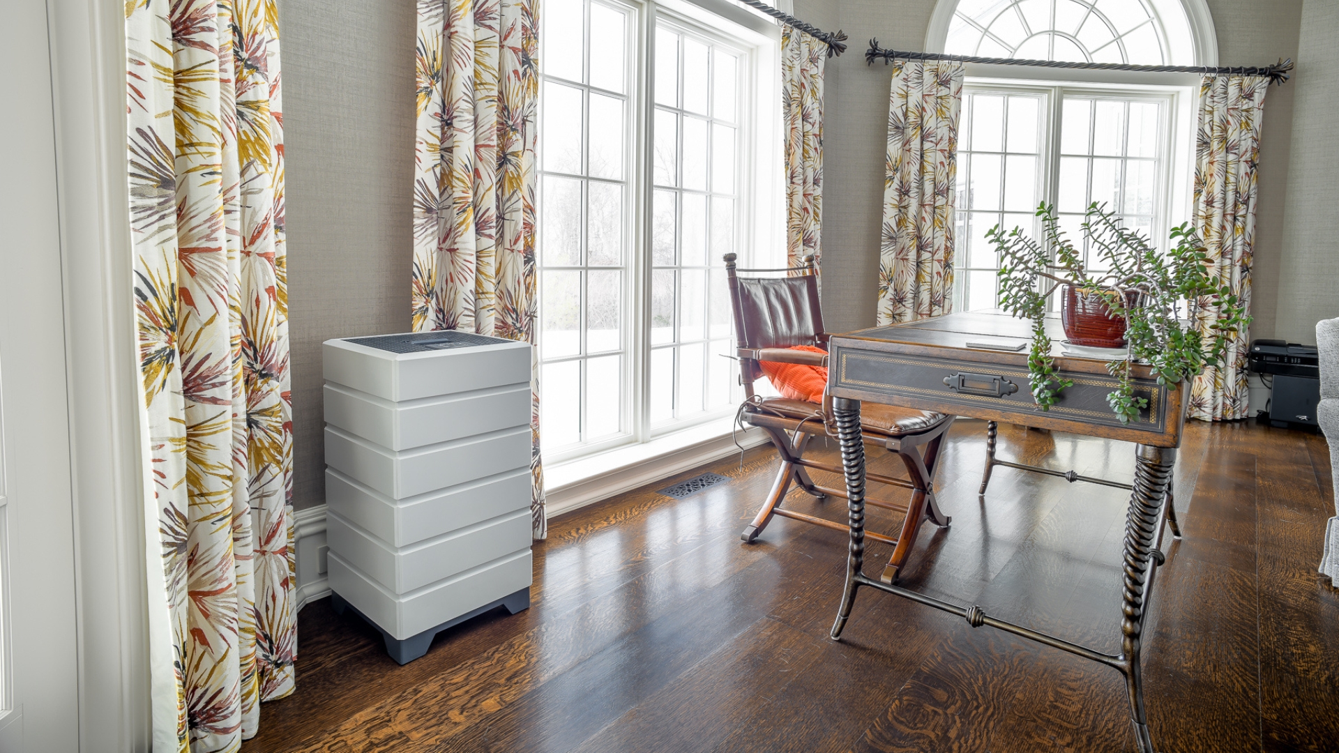 Photo of home with wood panel flooring and aged wood desk. In the left corner sits a white Aspen air purifier, installed by Basements Plus.