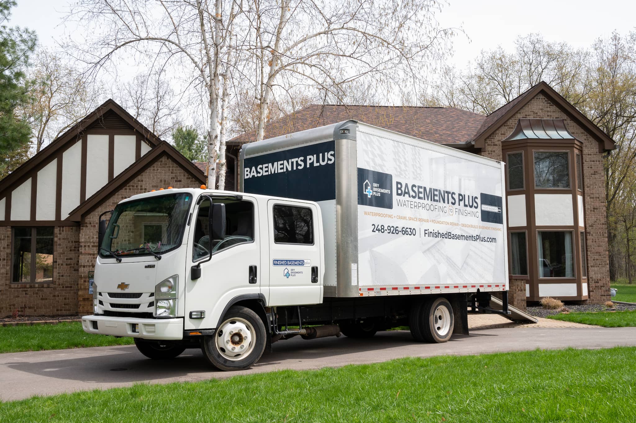 Photo of a Dry Basements Plus / Finished Basements Plus delivery truck parked in the driveway of a brick home with brown and white trim in Rochester.