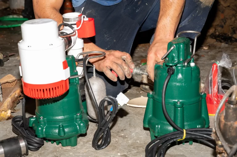 Basements Plus crew member preparing green sump pumps for installation.